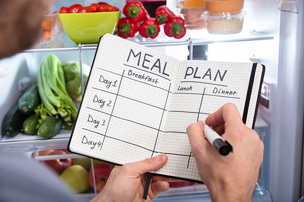  a diary with a meal plan for four days and view of a fridge in the backgroumd