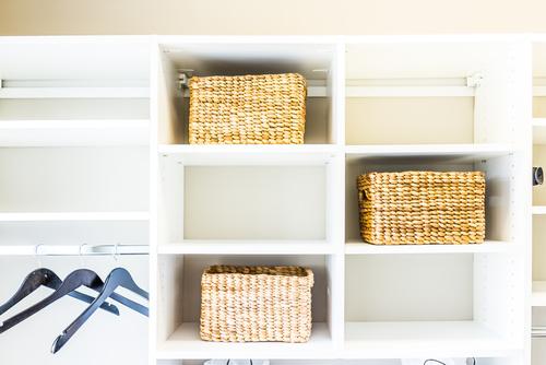 A tidy white closet organizer featuring several compartments; two have wicker baskets while others are empty. some empty hangers hang on a rod to the left.